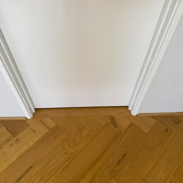 Herringbone flooring detailed where it meets a doorway and skirting