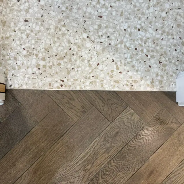 Smoked herringbone flooring meeting a terrazzo threshold
